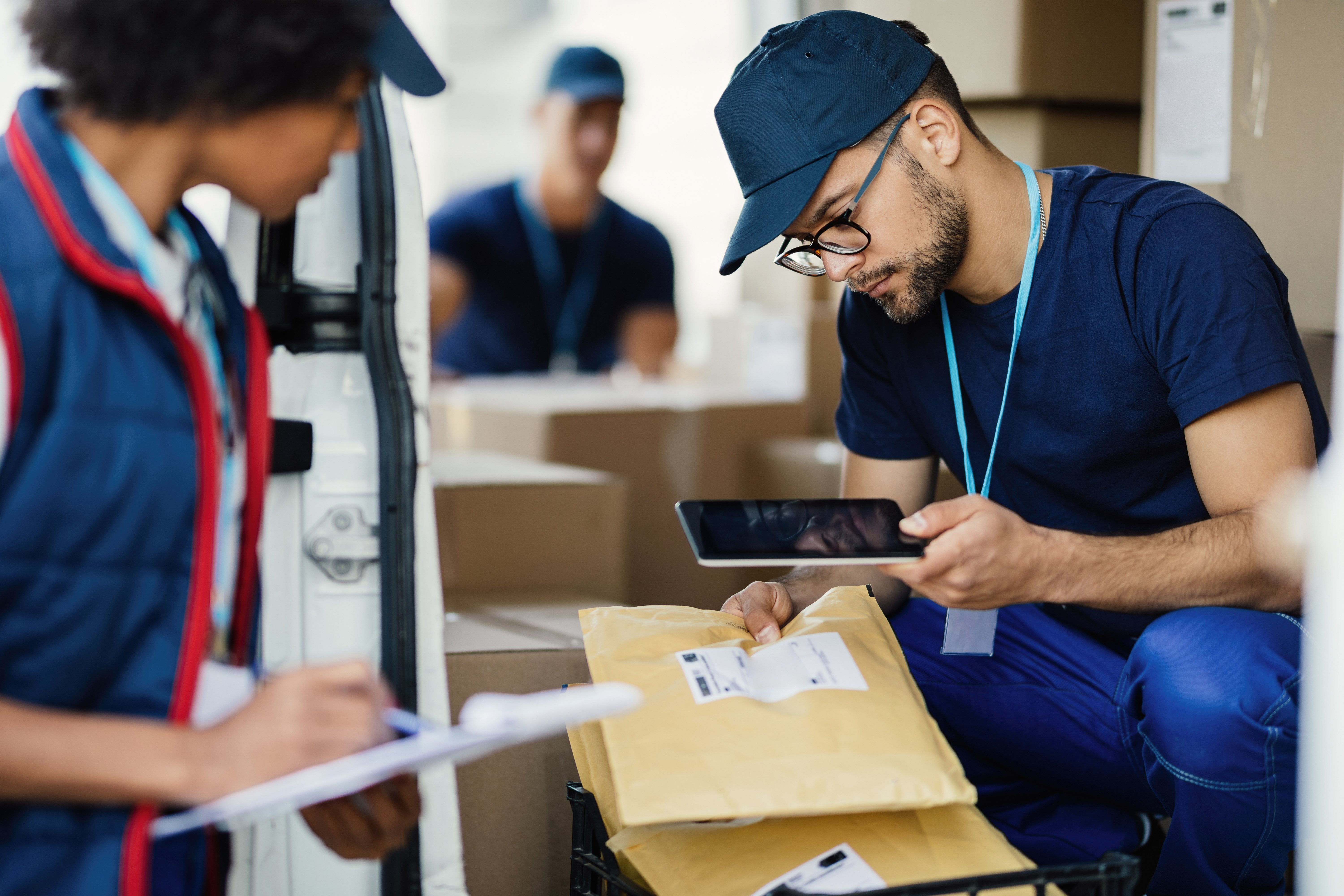 young-delivery-man-using-digital-tablet-scanning-bar-code-package-label-while-preparing-shipment-with-his-coworker